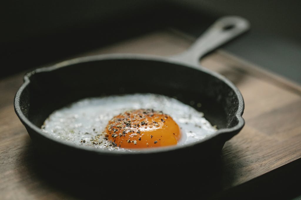 High angle of pan with fried egg with seasoning placed on wooden board in kitchen